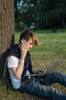 Dizüstü bilgisayar ve Ofis Binası yakınındaki parkta çalışma kulaklık genç adam