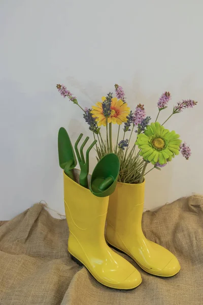 rain boots with gardening equipment and spring flowers on the eco background from sackcloth