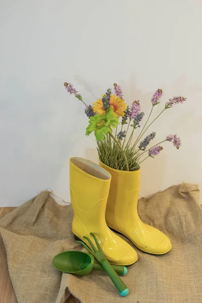 rain boots with gardening equipment and spring flowers on the eco background from sackcloth