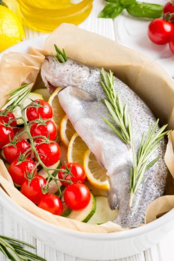 Akşam yemeği, kabak, domates bir şube, biberiye ve limon ile bir pişirme çanağı çiğ beyaz alabalık balık. Sağlıklı diyet gıda