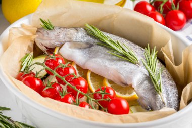 Akşam yemeği, kabak, domates bir şube, biberiye ve limon ile bir pişirme çanağı çiğ beyaz alabalık balık. Sağlıklı diyet gıda