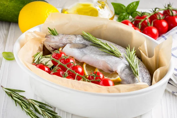 Akşam yemeği, kabak, domates bir şube, biberiye ve limon ile bir pişirme çanağı çiğ beyaz alabalık balık. Sağlıklı diyet gıda