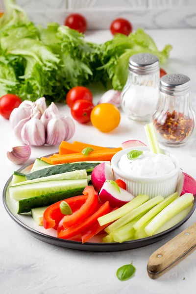 Tasty vegetable sticks of cucumber, pepper, carrots, celery and radishes with white sauce of sour cream, yogurt, herbs.