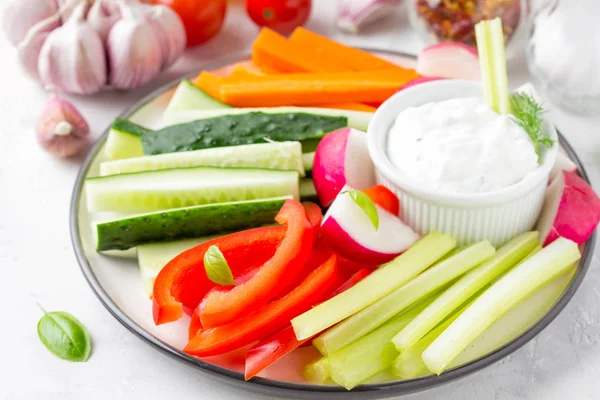 Tasty vegetable sticks of cucumber, pepper, carrots, celery and radishes with white sauce of sour cream, yogurt, herbs.