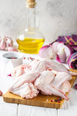 Bir kesme tahtası üzerinde çiğ tavuk kanatları. Yemek, baharat, soğan, yağ ve sarımsak için malzemeler