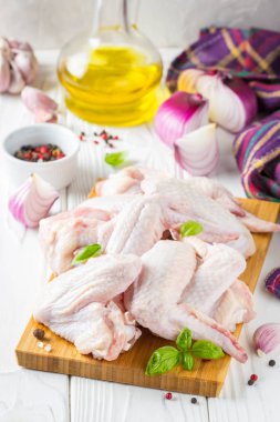 Bir kesme tahtası üzerinde çiğ tavuk kanatları. Yemek, baharat, soğan, yağ ve sarımsak için malzemeler