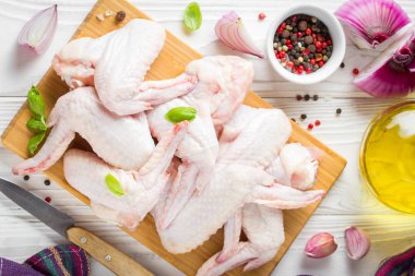 Bir kesme tahtası üzerinde çiğ tavuk kanatları. Yemek, baharat, soğan, yağ ve sarımsak için malzemeler
