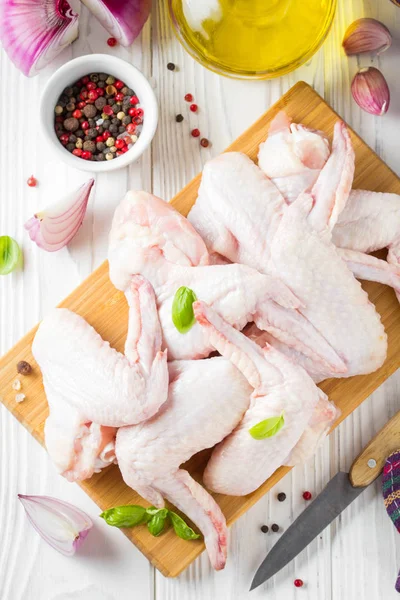 Bir kesme tahtası üzerinde çiğ tavuk kanatları. Yemek, baharat, soğan, yağ ve sarımsak için malzemeler
