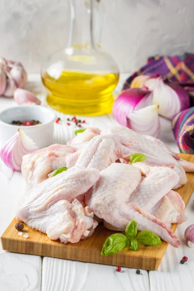 Bir kesme tahtası üzerinde çiğ tavuk kanatları. Yemek, baharat, soğan, yağ ve sarımsak için malzemeler