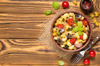 İtalyan pasta kızarmış sebze ve mantar, kabak, domates, champignon, peynir ve fesleğen. Ahşap arka plan üzerinde koyu kase