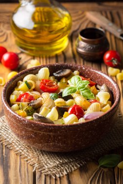 İtalyan pasta kızarmış sebze ve mantar, kabak, domates, champignon, peynir ve fesleğen. Ahşap arka plan üzerinde koyu kase