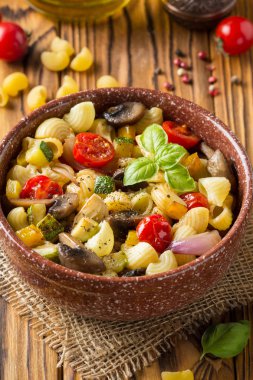 İtalyan pasta kızarmış sebze ve mantar, kabak, domates, champignon, peynir ve fesleğen. Ahşap arka plan üzerinde koyu kase