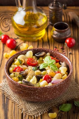 İtalyan pasta kızarmış sebze ve mantar, kabak, domates, champignon, peynir ve fesleğen. Ahşap arka plan üzerinde koyu kase