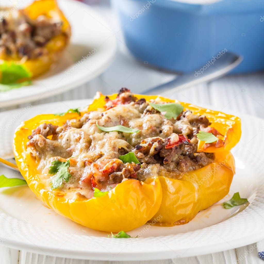 Stuffed yellow bell peppers, beef stew stuffing with vegetables and cheese. Light wooden background