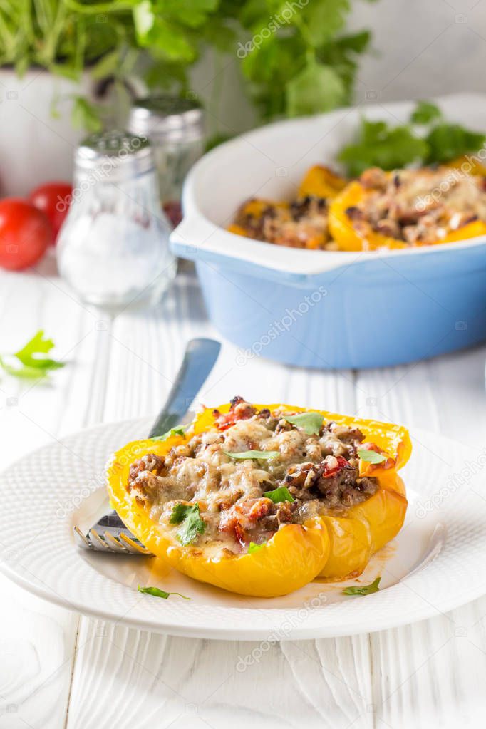 Stuffed yellow bell peppers, beef stew stuffing with vegetables and cheese. Light wooden background