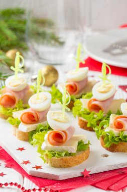 Noel kanepeler üzerinde brie veya Camembert peyniri, jambon ve bıldırcın haşlanmış yumurta ile ekmek. Yeni yıl'ın masada güzel tanıtımı. Stick lezzetli starter