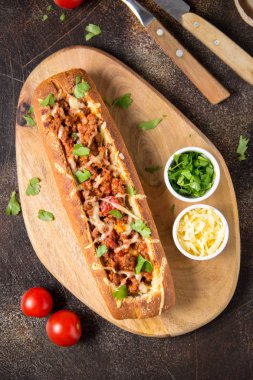 Baget bolognese yahni, kıyma, domates ve peynir ile doldurulmuş. Lezzetli bir öğle yemeği İtalyanca, lezzetli aperatifler, koyu arka plan üzerinde ev yapımı sandviç