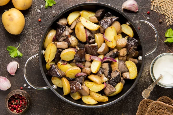 Fried potatoes with forest mushrooms, boletus, onions and sour cream. Rustic dish in a frying pan, vegetarian autumn food on top of view