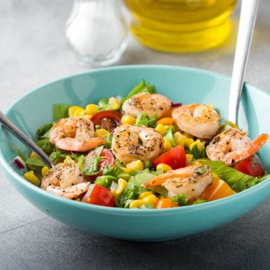 Mısır, yağda kızartılmış karides, cherry domates, kırmızı soğan ve mavi tabak taze lezzetli yemek, sağlıklı gıda içinde marul salatası