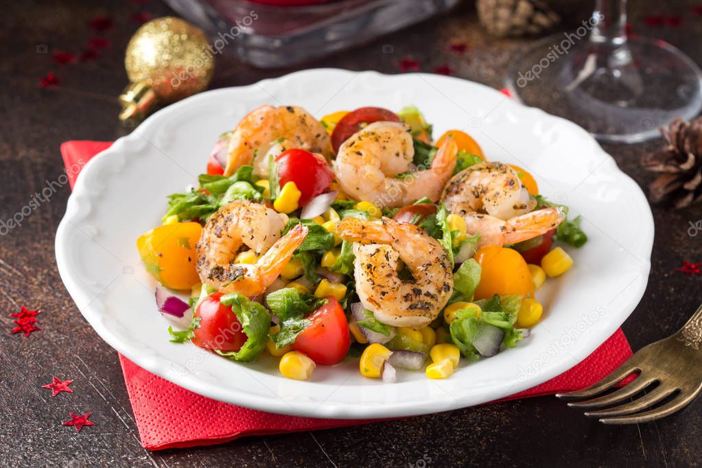 Salad with corn, fried shrimp, cherry tomatoes, red onions and lettuce on  white plate. Appetizer for Christmas party on dark background