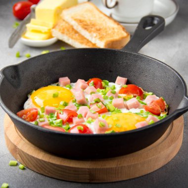 Jambon, domates ve yeşil soğan ile siyah tavada kızarmış yumurta. Kızarmış ekmek ve tereyağı ile lezzetli Breakfast. Klasik İngilizce