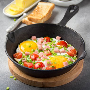 Jambon, domates ve yeşil soğan ile siyah tavada kızarmış yumurta. Kızarmış ekmek ve tereyağı ile lezzetli Breakfast. Klasik İngilizce