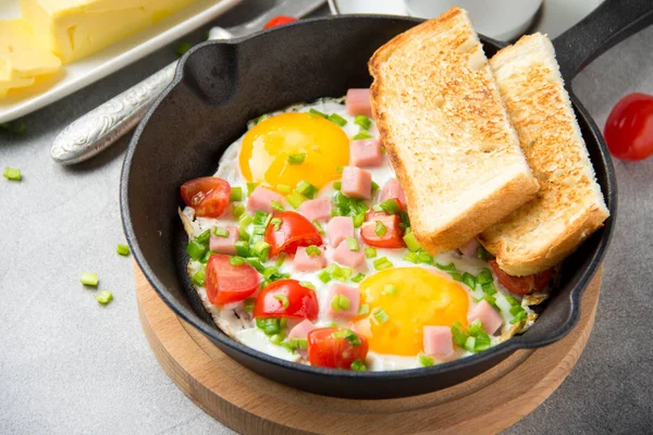 Jambon, domates ve yeşil soğan ile siyah tavada kızarmış yumurta. Kızarmış ekmek ve tereyağı ile lezzetli Breakfast. Klasik İngilizce