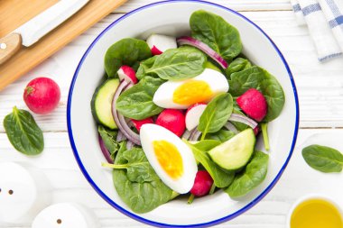 Taze bahar ıspanak, turp, salatalık ve yumurta salatası. Lezzetli yemek, sağlıklı gıda, yaz sebze. Beyaz ahşap zemin üzerinde kase