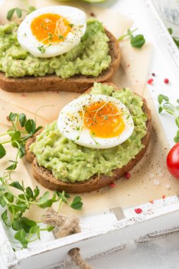 Beyaz tepside avokado püresi ve yumuşak haşlanmış yumurta ile tost, sıvı