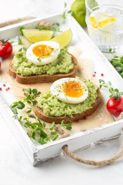Beyaz tepside avokado püresi ve yumuşak haşlanmış yumurta ile tost, sıvı
