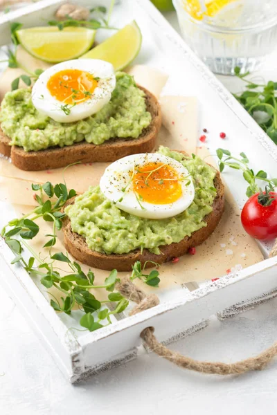 Toast met avocado puree en zachtgekookt ei op witte dienblad, liqu — Stockfoto