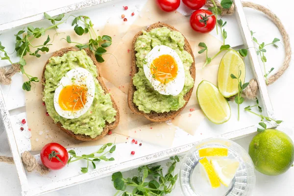 Toast met avocado puree en zachtgekookt ei op witte dienblad, liqu — Stockfoto