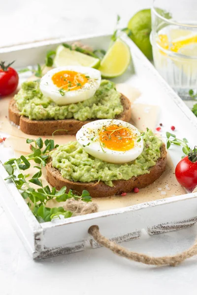 Tostadas con puré de aguacate y huevo cocido en bandeja blanca, liqu —  Fotos de Stock