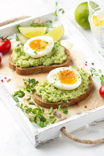 Toast met avocado puree en zachtgekookt ei op witte dienblad, liqu — Stockfoto