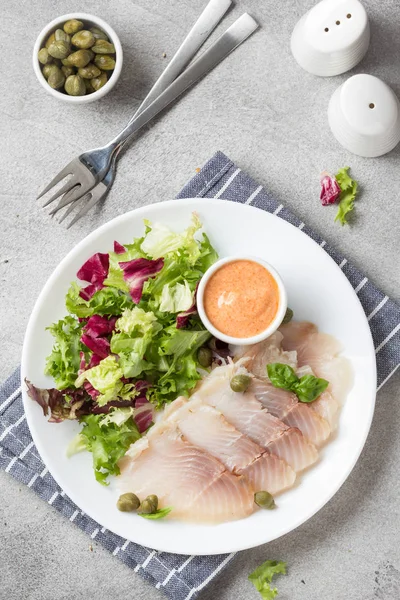 Thin slices of salted smoked fish with lettuce leaves and sauce. — Stock Photo, Image