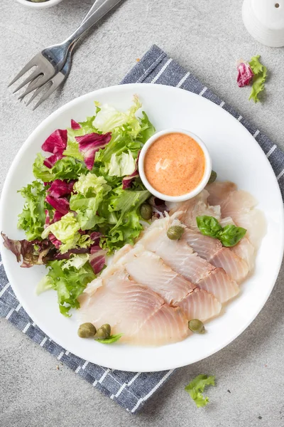 Thin slices of salted smoked fish with lettuce leaves and sauce. — Stock Photo, Image