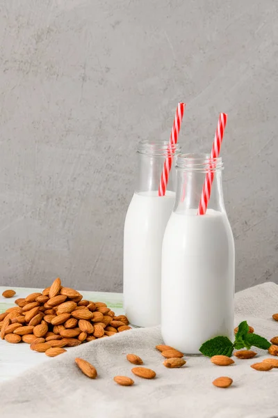 Bottle of milk from almonds on a white wooden table, with almonds and green