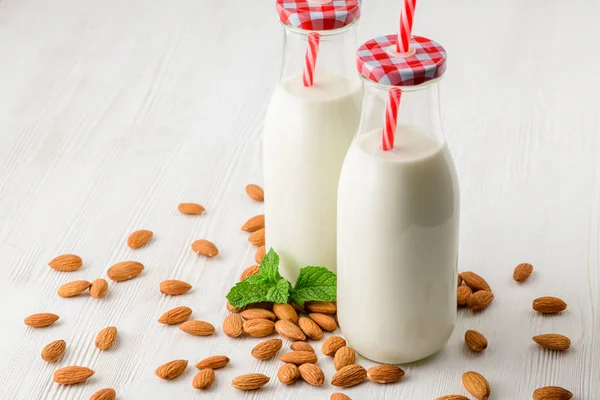 Bottle of milk from almonds on a white wooden table, with almonds and green.