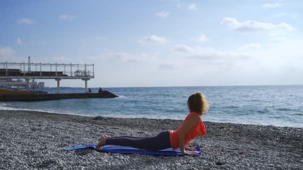 Flicka nära havet gör yoga på en strand vid soluppgången — Stockvideo