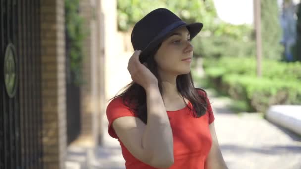 Mooi meisje poseert voor de camera. Jong mooi meisje met groene ogen in een rood T-shirt en zwarte hoed poseren op camera in de zomer — Stockvideo