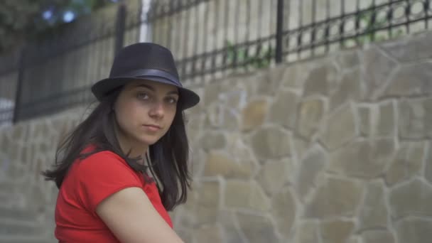 Bella ragazza posa sulla fotocamera. Giovane bella ragazza con gli occhi verdi in una maglietta rossa e cappello nero posa sulla fotocamera in estate — Video Stock