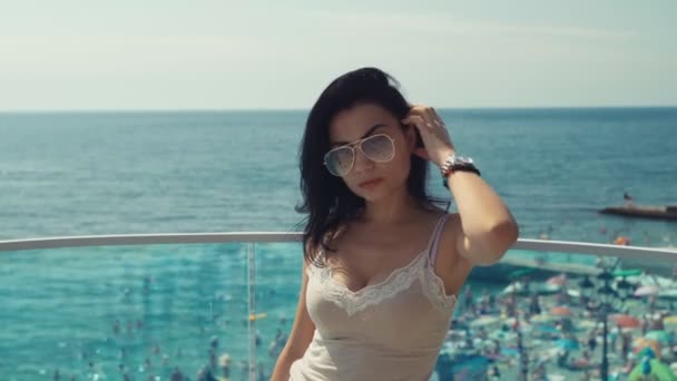 Hermosa morenita vestida de gafas de sol que se pone y baila a la cámara en un fondo del mar. — Vídeo de stock