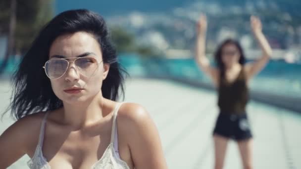 两个戴着太阳镜的漂亮的黑发女孩 一个是背景中的特写 另一个是4K — 图库视频影像