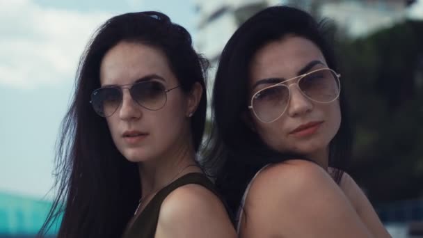 Zwei Schöne Brünette Mädchen Mit Sonnenbrille Sitzen Rücken Rücken Und — Stockvideo