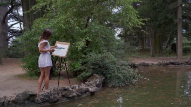 Parkta Kız sanatçı bir lotus 4k ile küçük bir eski gölet boyalar yağlı boyalar ile bir manzara boyar