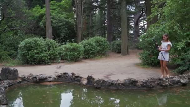 女の子アーティストは 小さな池4Kで公園で風景画のための紙パレットやペイントブラシを準備します — ストック動画
