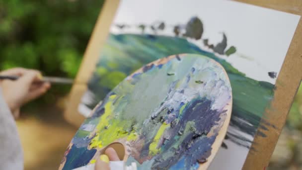 パレット上の女の子アーティストは 古い小さな池4Kの風景をペイントするために小さな塗料を広げる — ストック動画