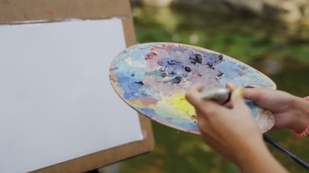 Chica artista en el parque pinta un paisaje con pinturas al óleo un pequeño estanque viejo 4k — Vídeos de Stock