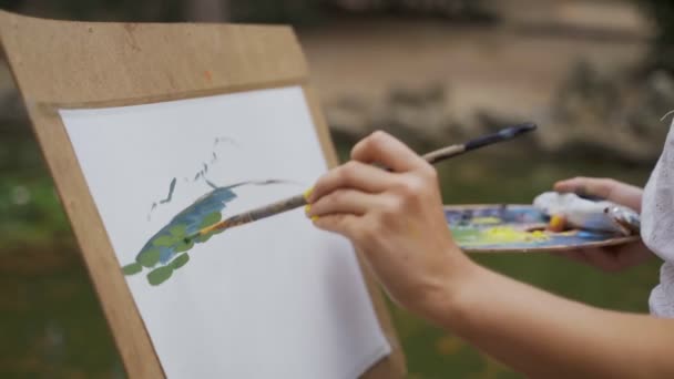 Chica artista en el parque pinta un paisaje con pinturas al óleo un pequeño estanque viejo 4k — Vídeos de Stock