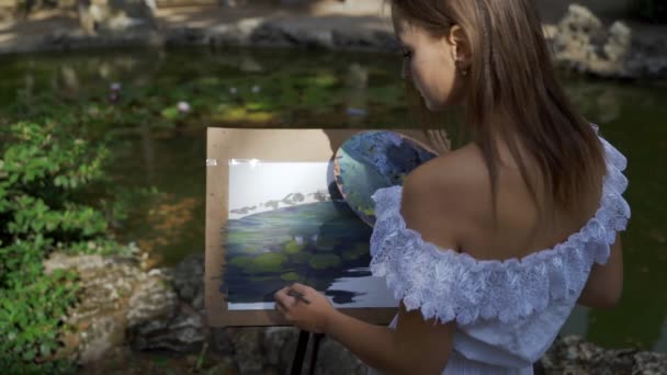 Girl artist in the park paints a landscape with oil paints a small old pond 4k — Stock Video